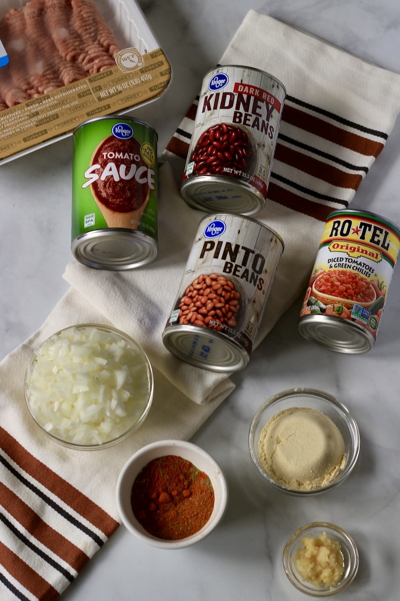 Ingredients for Frito pie on a counter with a white and orange striped dish towel.