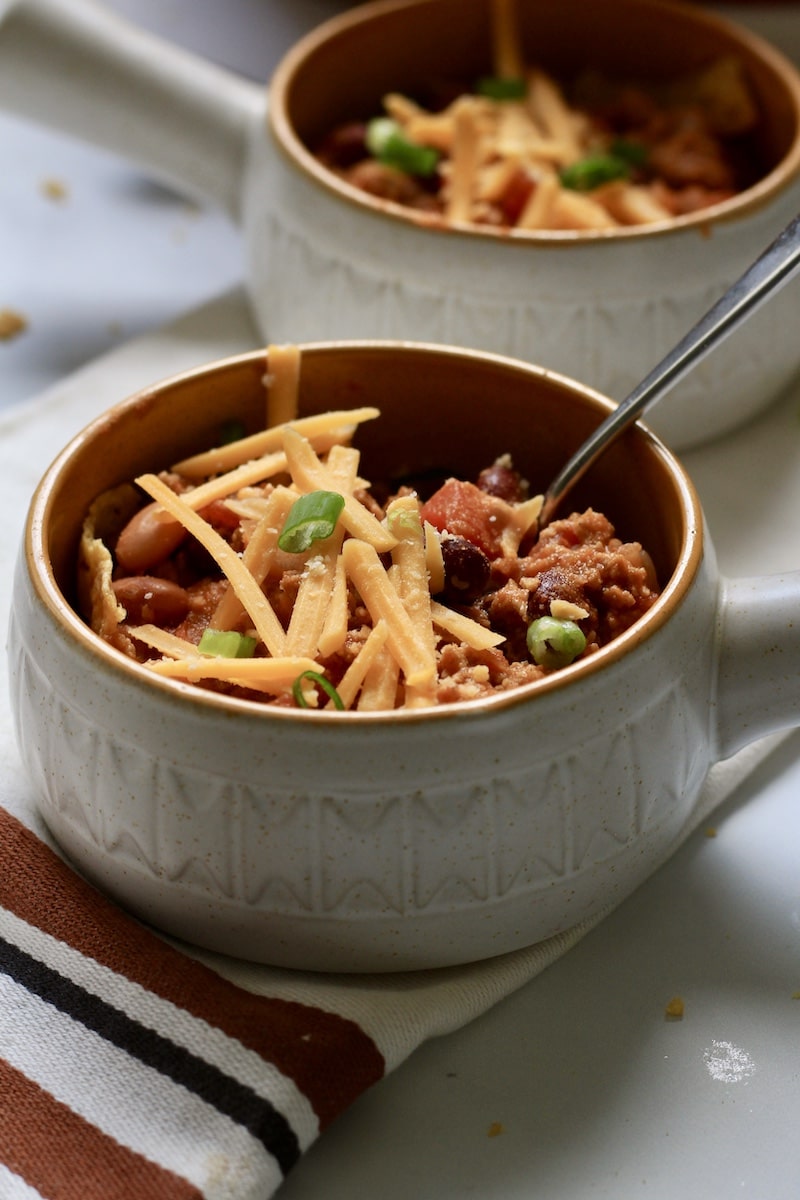 From the side photo of frito pie in two bowls topped with cheese and green onion and a silver spoon in the bowl.