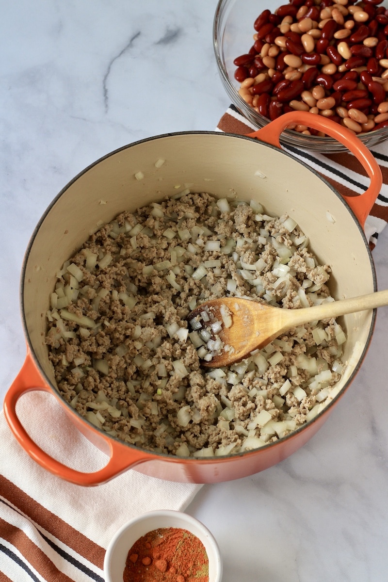 A large orange pot with cooked ground meat and onions with a bowl of beans in the top right.
