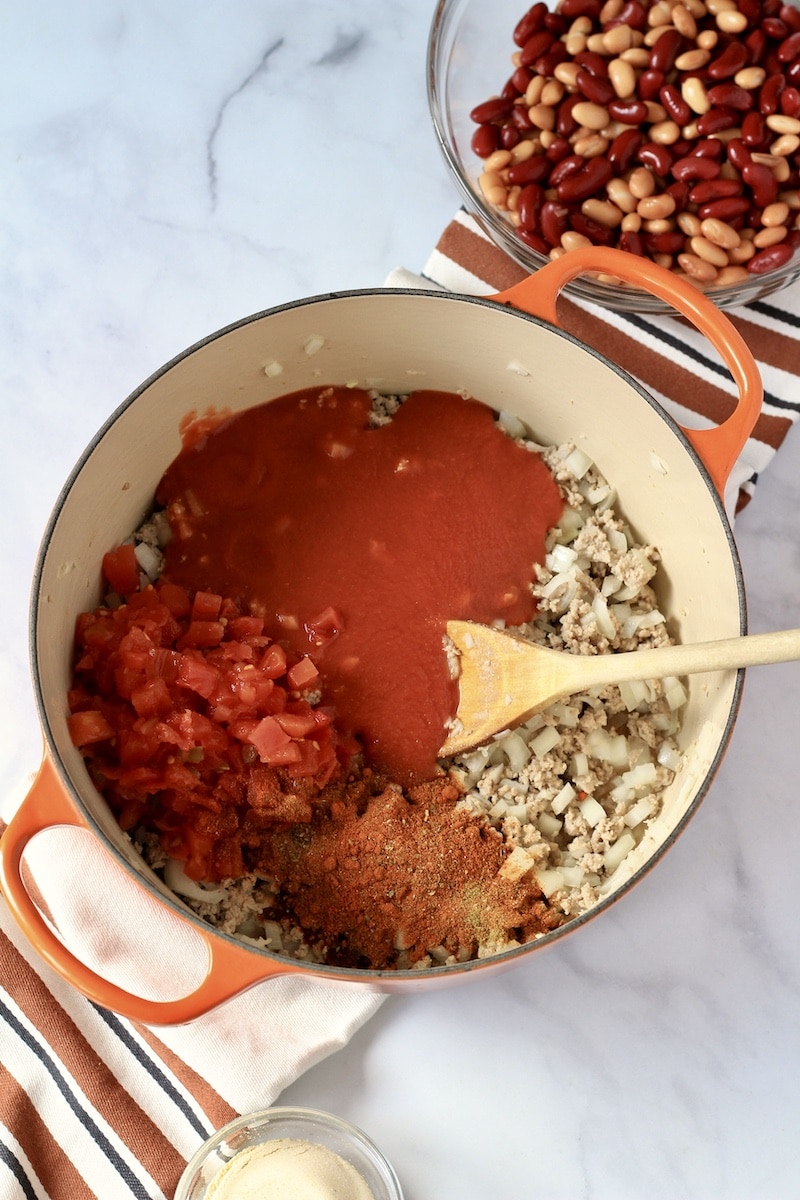 A large orange pot with ground meat, tomato sauce, rotel, and spices.