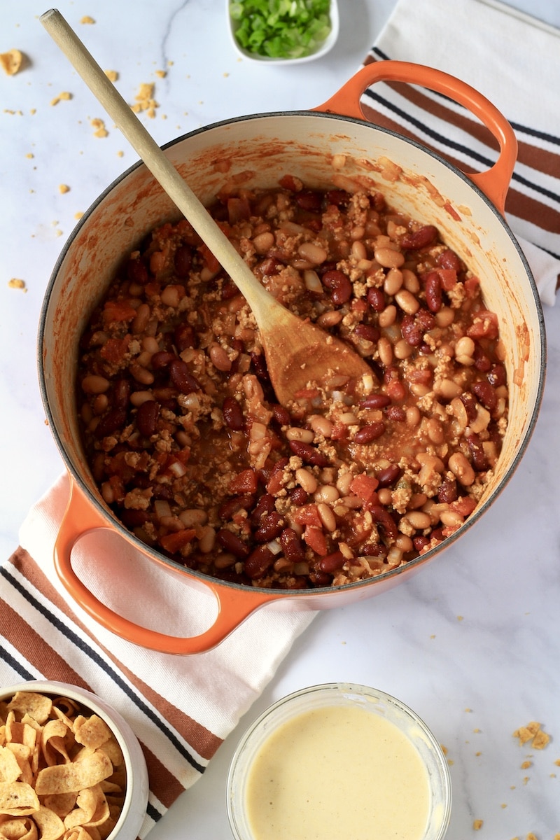 A large orange pot with cooked meat and beans for chili.
