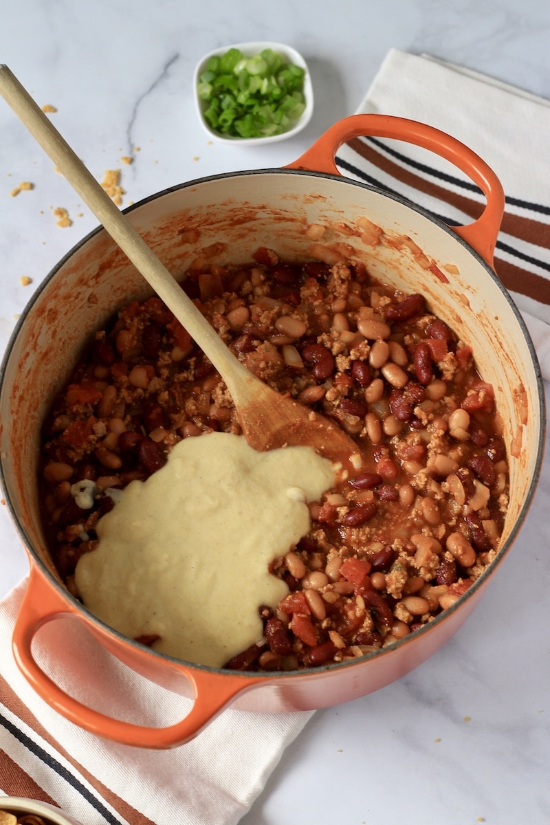 A large orange pot of chili with the corn slurry on top.