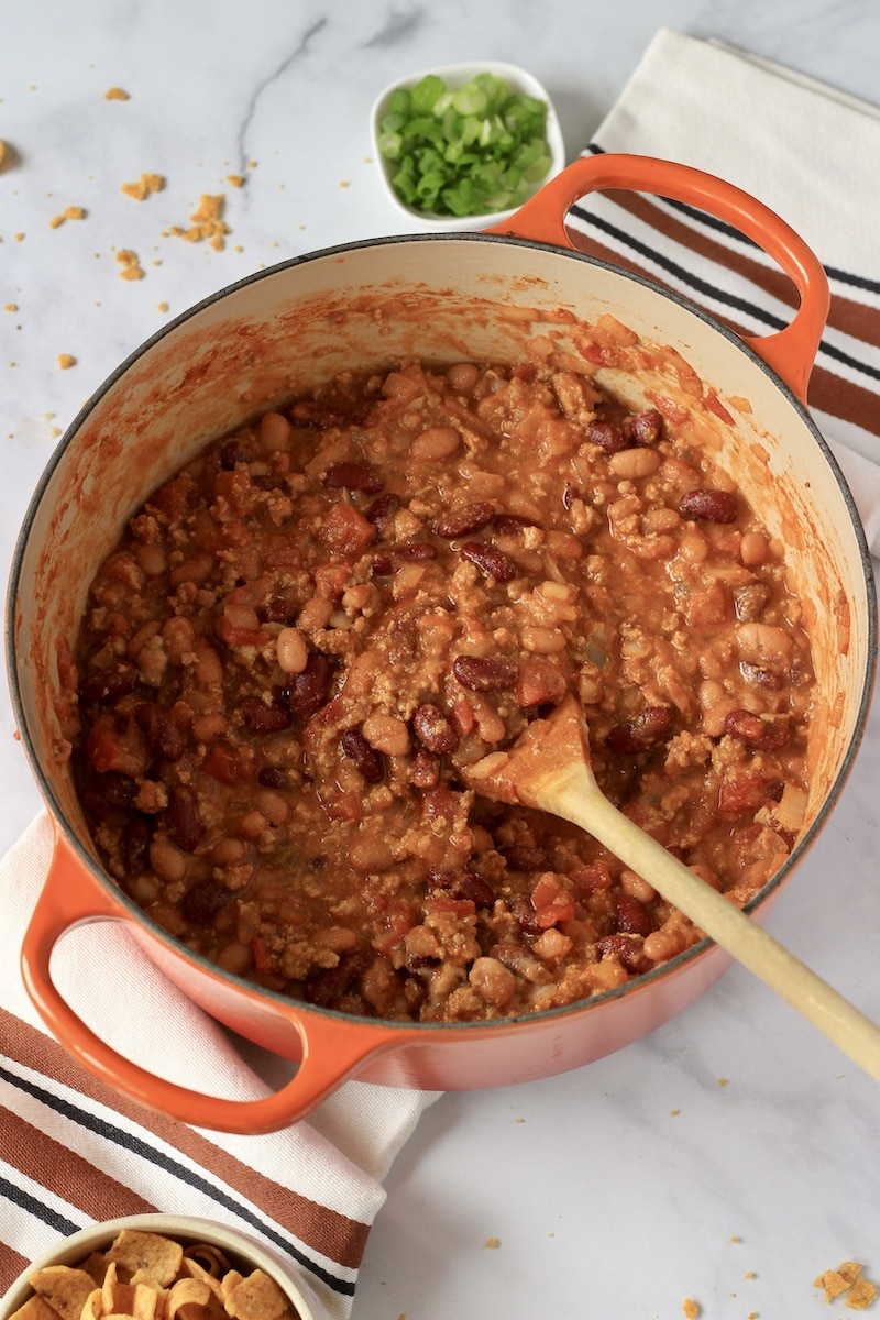 A large orange pot of chili with a wooden spoon.