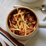 A top down photo of a bowl of frito pie topped with vegan cheese and green onion in a small bowl.