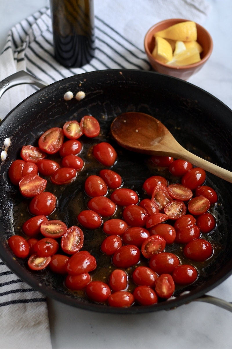 A skillet with grape tomatoes roasting with a wooden spoon.