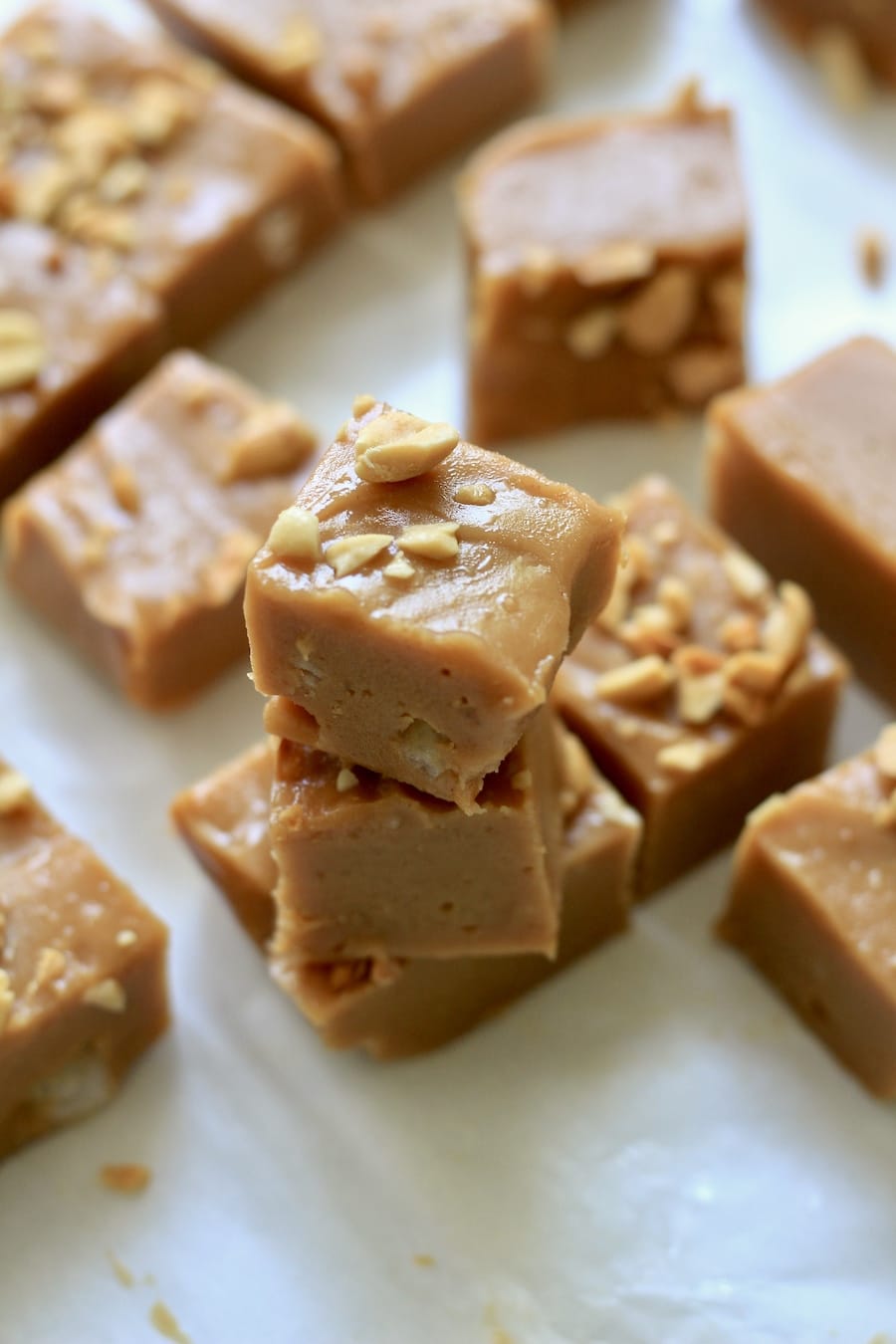 A parchment paper lined counter topped with a stack of peanut butter fudge cut into squares.