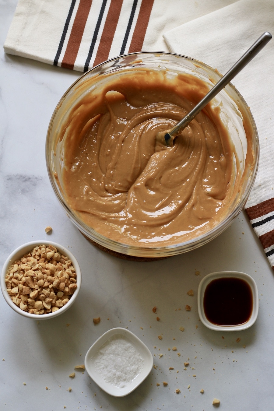 A large bowl with melted peanut butter and sweetened condensed coconut milk with a spatula and other ingredients below.