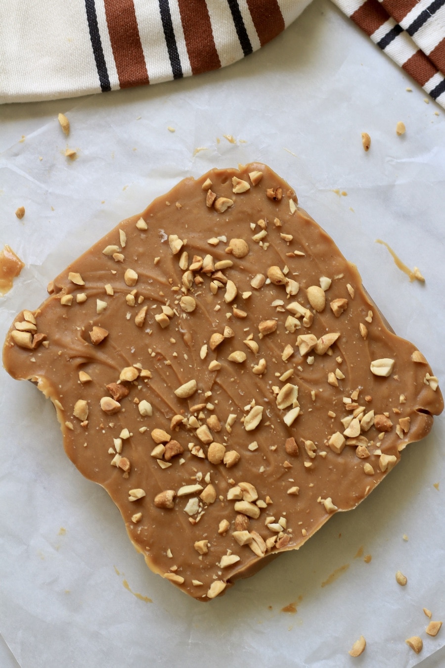 Peanut topped peanut butter fudge on a white counter with peanuts sprinkled around.