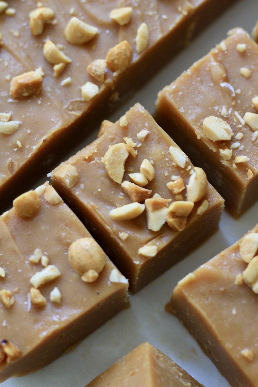 Sliced squares of peanut butter fudge topped with chopped peanuts on parchment paper.
