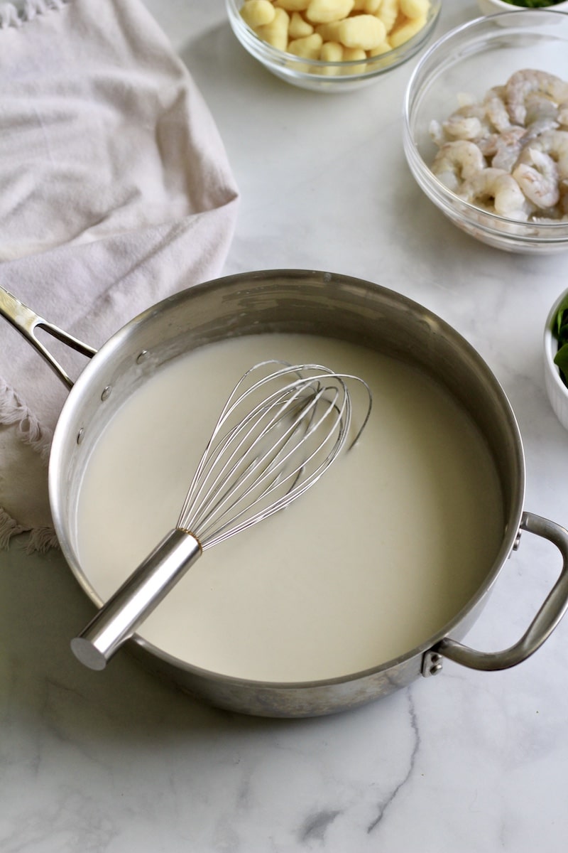A silver skillet with a whisk filled with the creamy sacue.