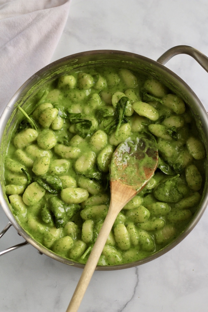 Creamy pesto gnocchi with a wooden spoon in a silver skillet.