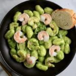 A top down photo of creamy pesto gnocchi with a slice of bread on the plate.