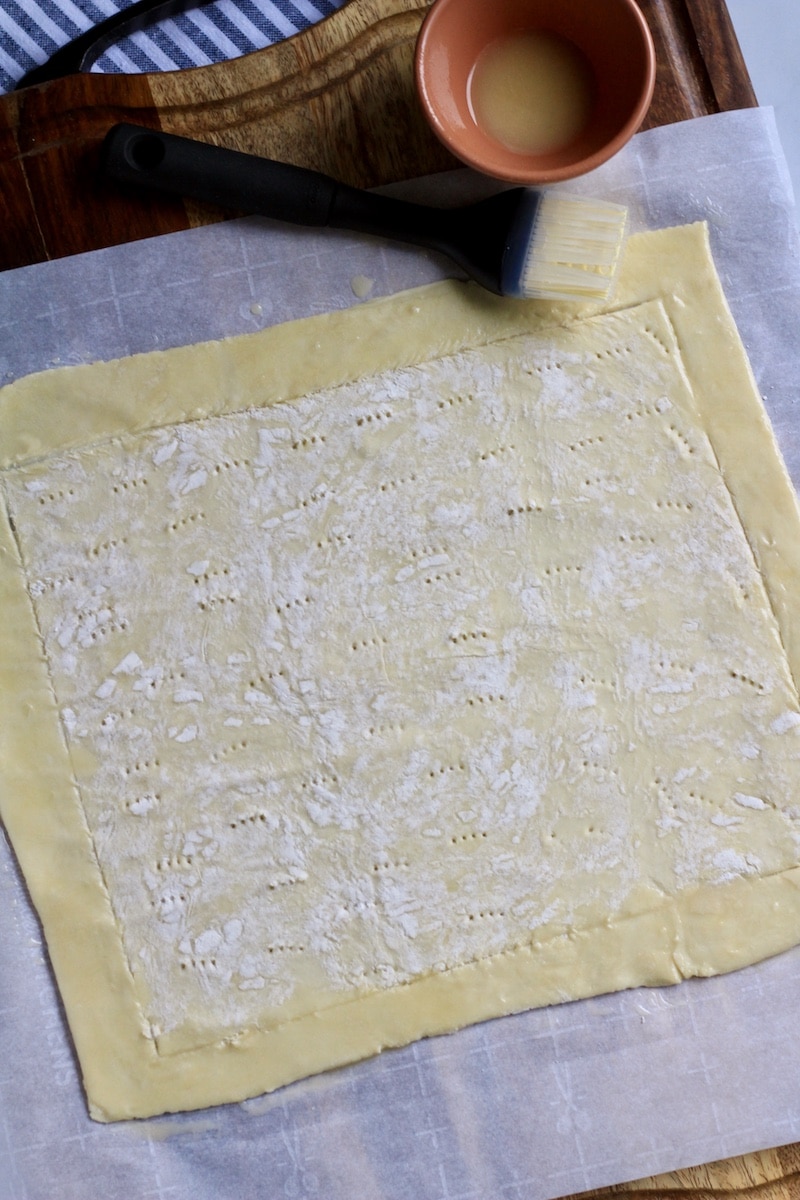 A parchment paper with puff pastry after rolling out and scoring the edges.