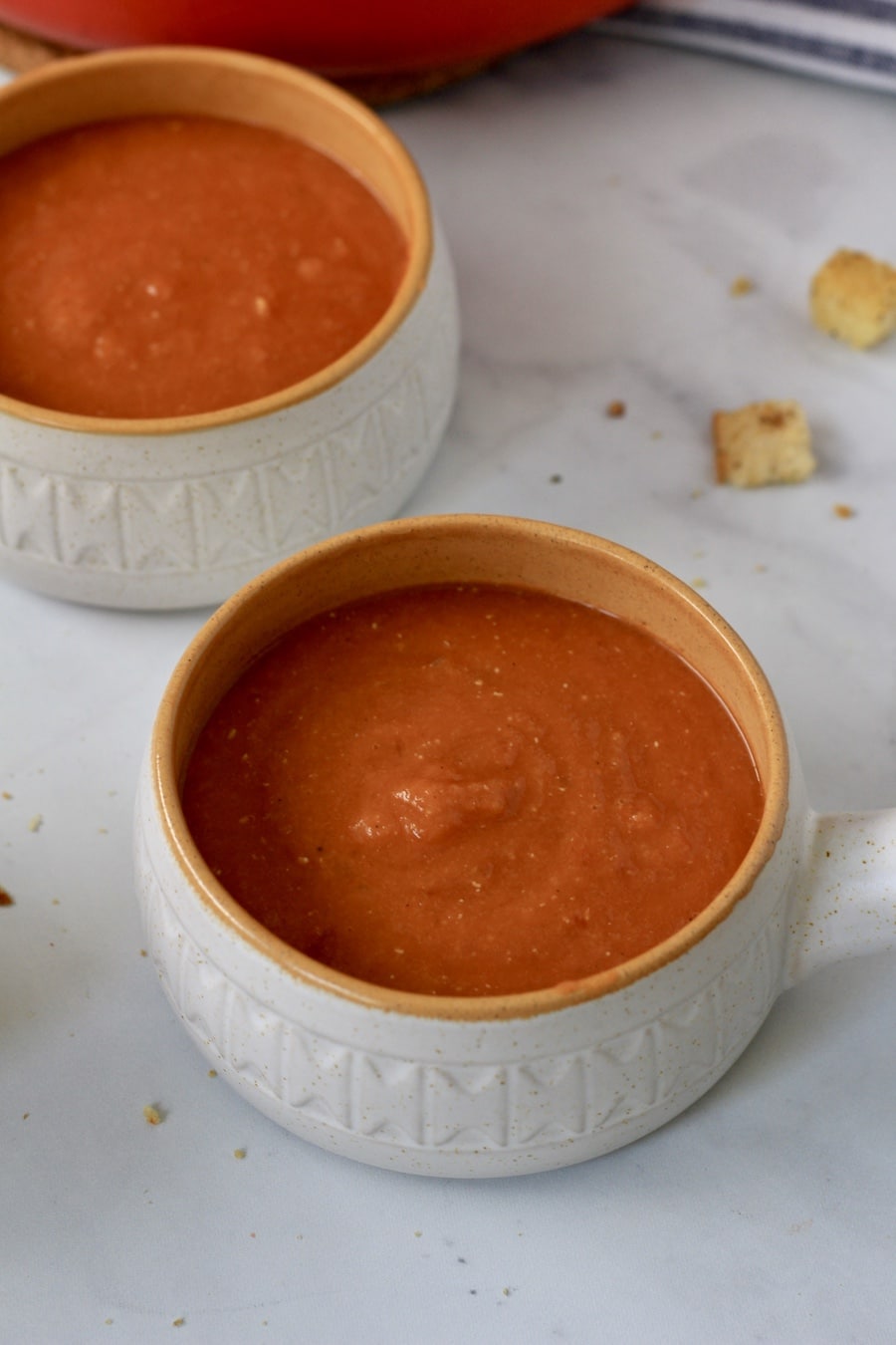 Two small orange rimmed bowls filled with tomato lentil soup.
