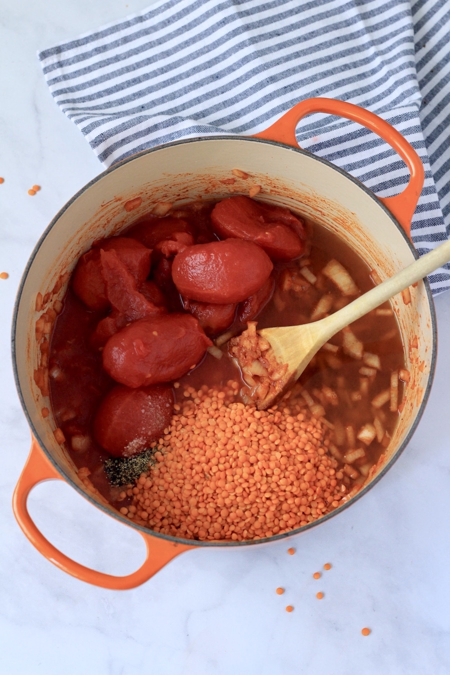 An orange dutch oven with all of the tomato lentil soup ingredients before simmering.