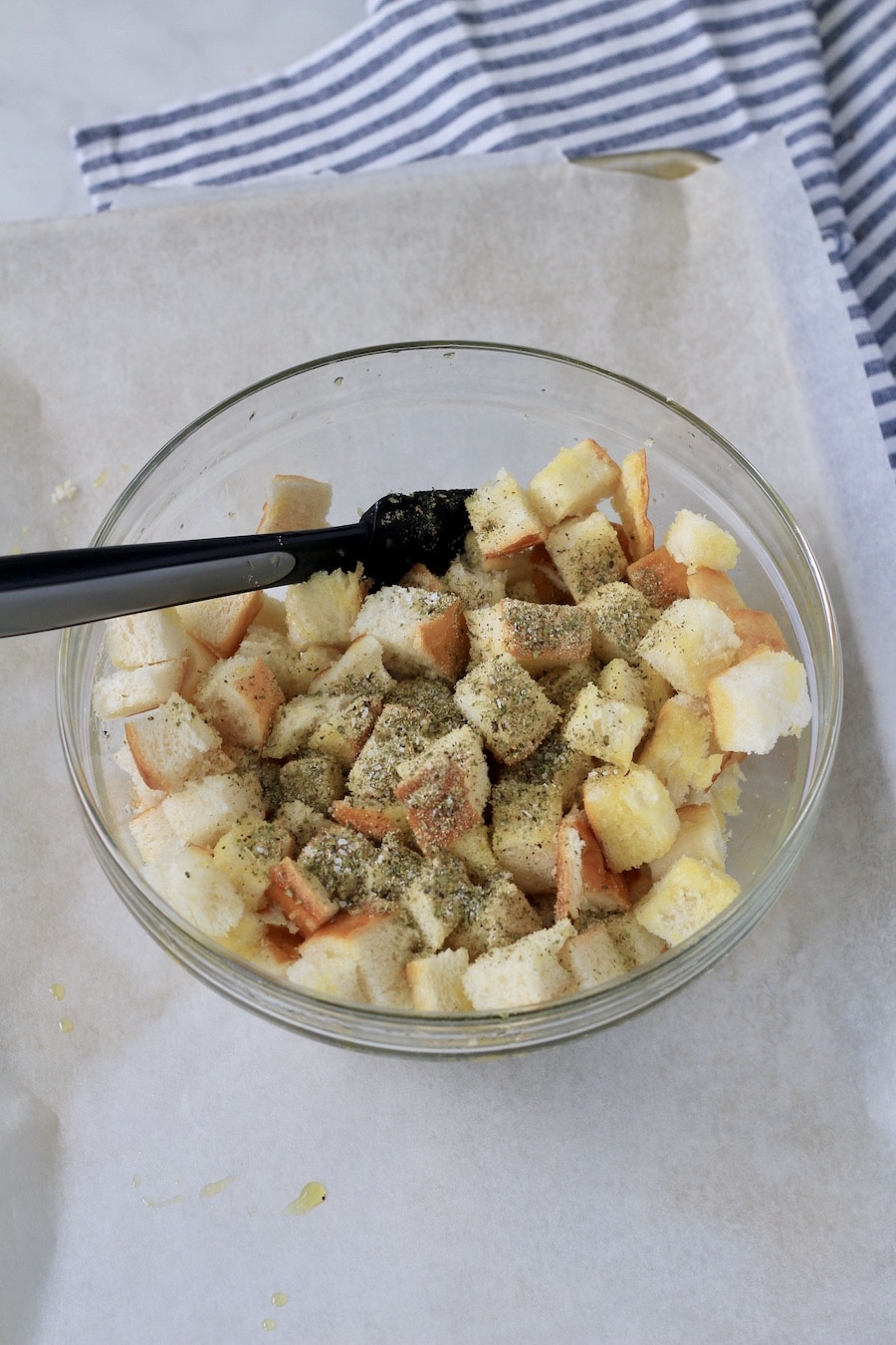 A medium-sized bowl with croutons and seasoning before mixing together.