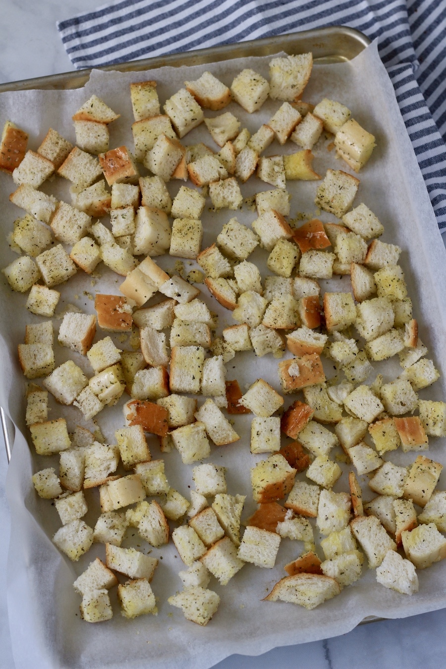 A parchment paper lined baking sheet with seasoned croutons before baking.