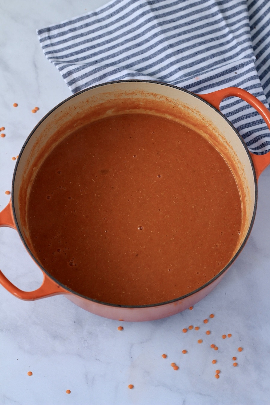 An orange dutch oven with blended vegan tomato lentil soup.