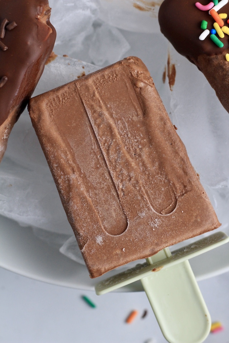 A plain vegan fudgesicle sitting in a bowl of ice.