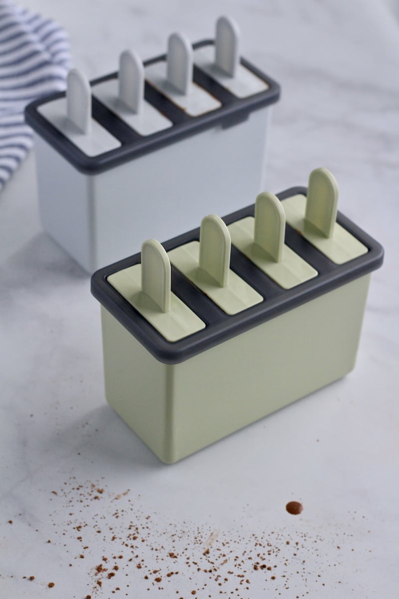 Two mini popsicle molds filled with vegan fudgesicles and topped with popsicle sticks.