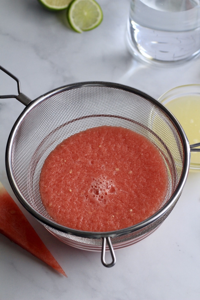 A glass bowl with a strainer, straining the watermelon juice.
