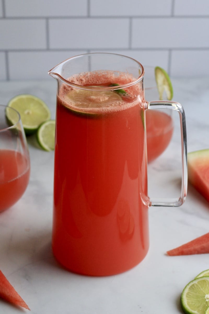 A glass pitcher of fresh squeezed watermelon limeade on a white counter.
