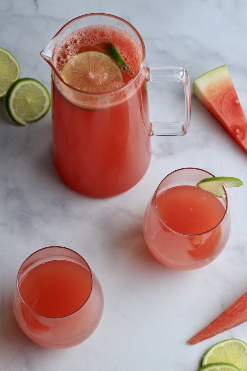 A top down photo of watermelon limeade in a pitcher with two glasses of limeade in the front.