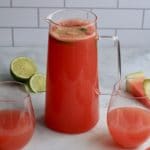A square picture of a pitcher of watermelon limeade with a glass of limeade to the left and the right.