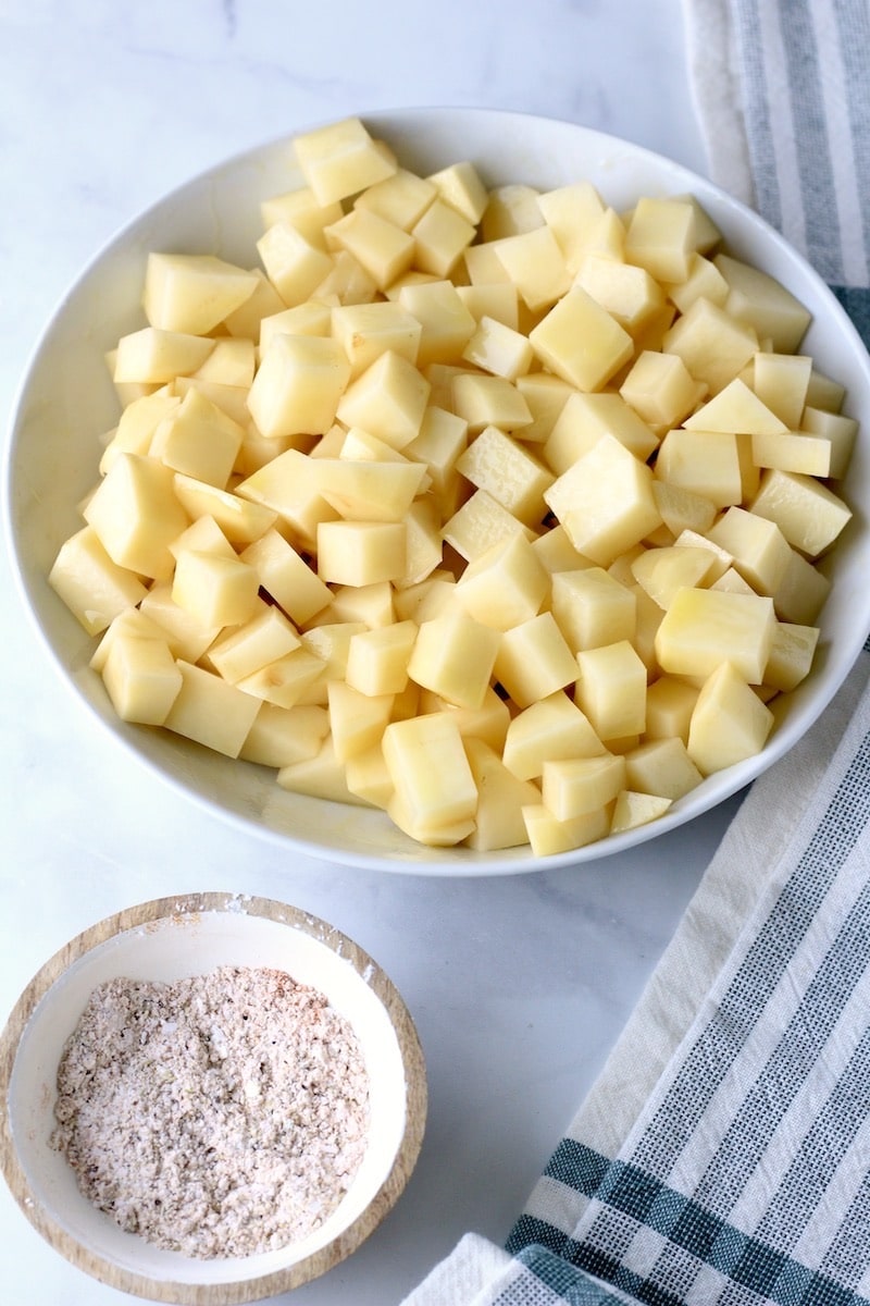 Two bowls on a counter one with diced potatoes and the other with seasoning blend.