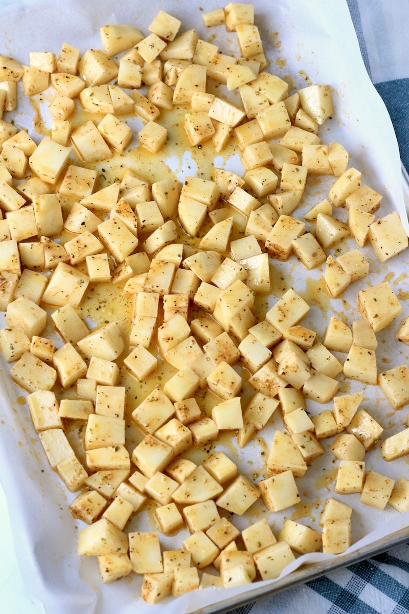 A parchment paper lined baking sheet with seasoned breakfast potatoes before baking.