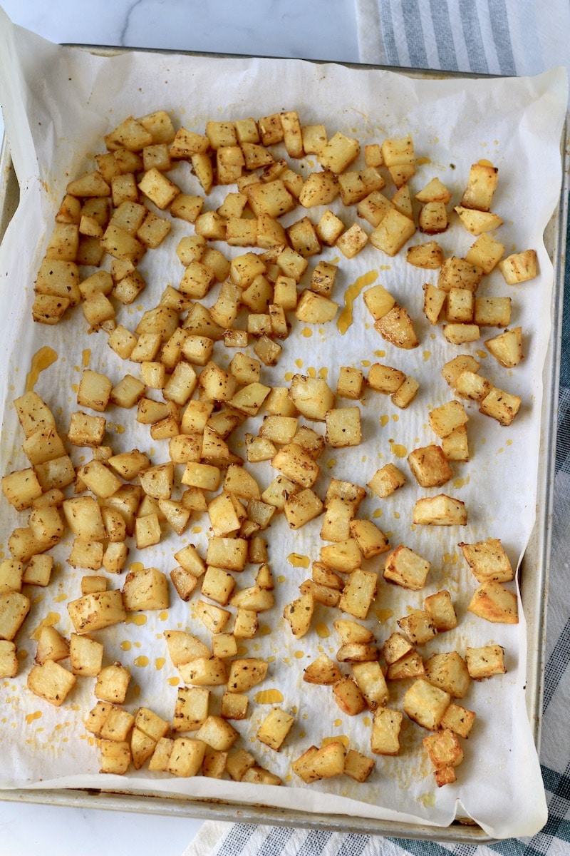 A parchment paper lined baking sheet with roasted breakfast potatoes during baking.