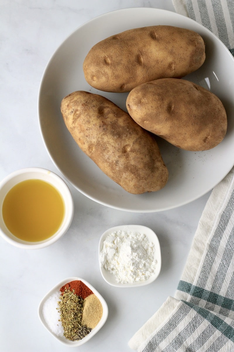 Ingredients for breakfast potatoes on a white counter with a green and white towel.