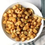 A white bowl with a gold spoon filled with oven-roasted breakfast potatoes.