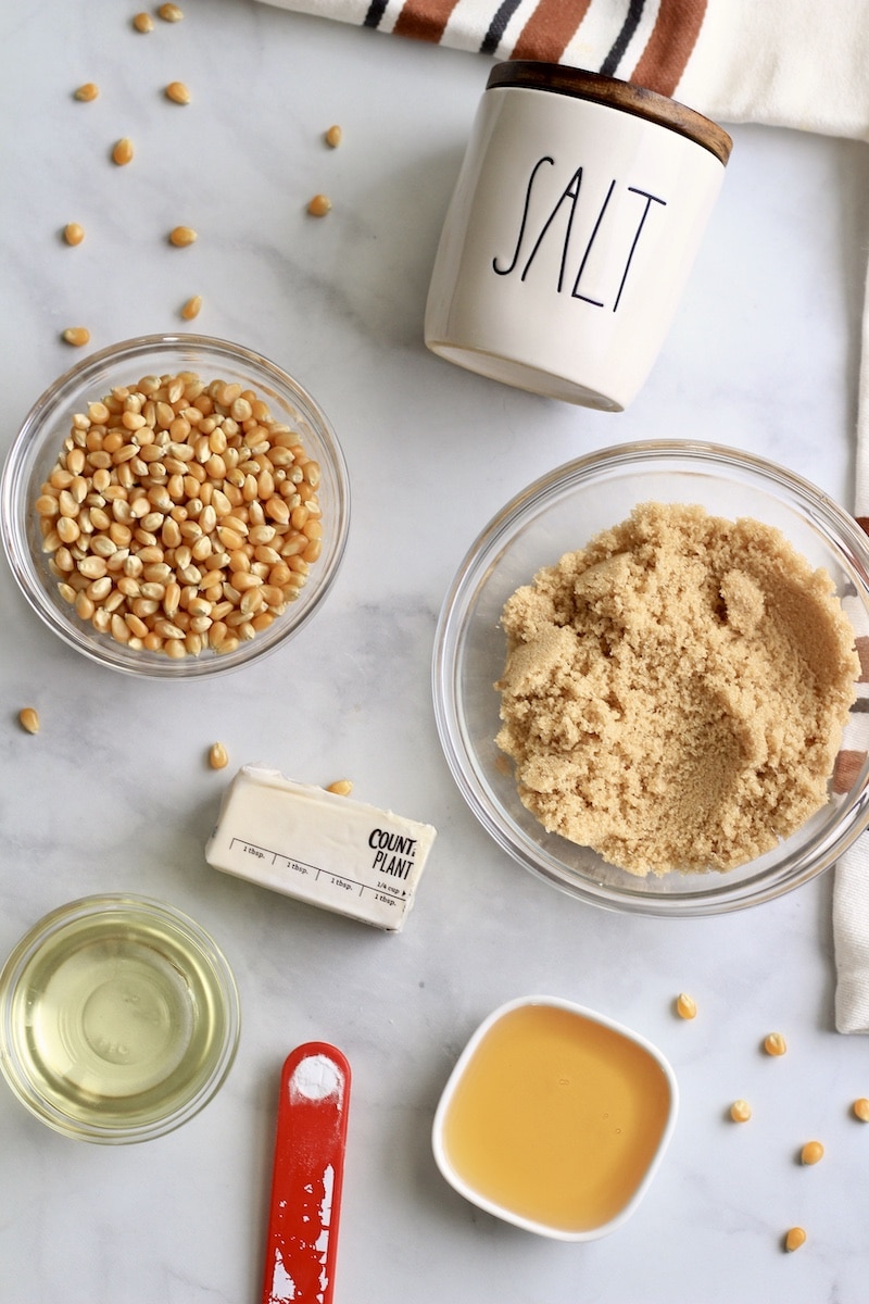 Ingredients for caramel corn on a white counter with popcorn kernels scattered around.