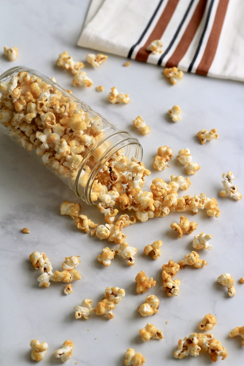 A glass jar of caramel corn that has spilled on the counter.