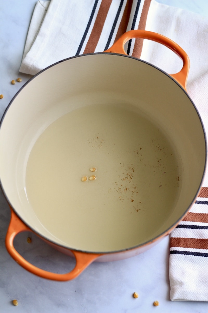 A dutch oven with coconut oil and three popcorn kernels before heating.