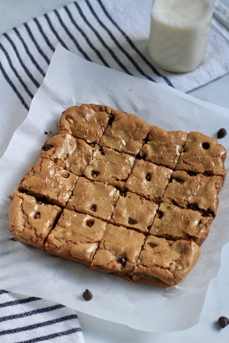 Chocolate chip blondies on parchment paper after baking with a jar of oat milk in the back.