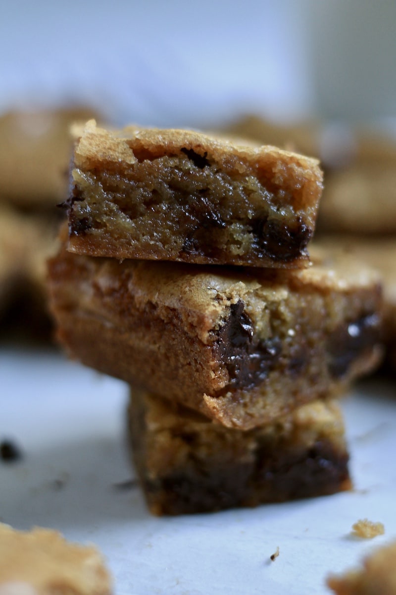 Three chocolate chip blondies in a stack with the gooey center showing.