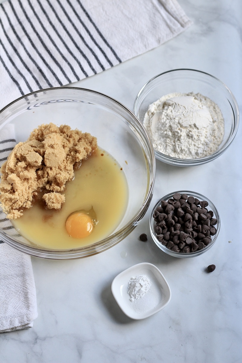 Bowl with butter, sugar, and egg on the left, bowls with flour, chocolate chips, and baking soda on the right.
