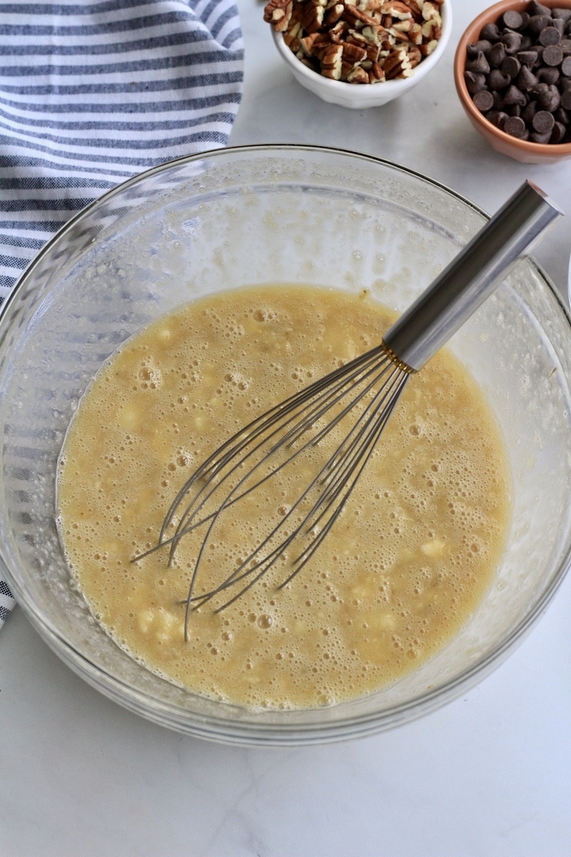 A large glass bowl with a wire whisk and the wet ingredients all mixed together.