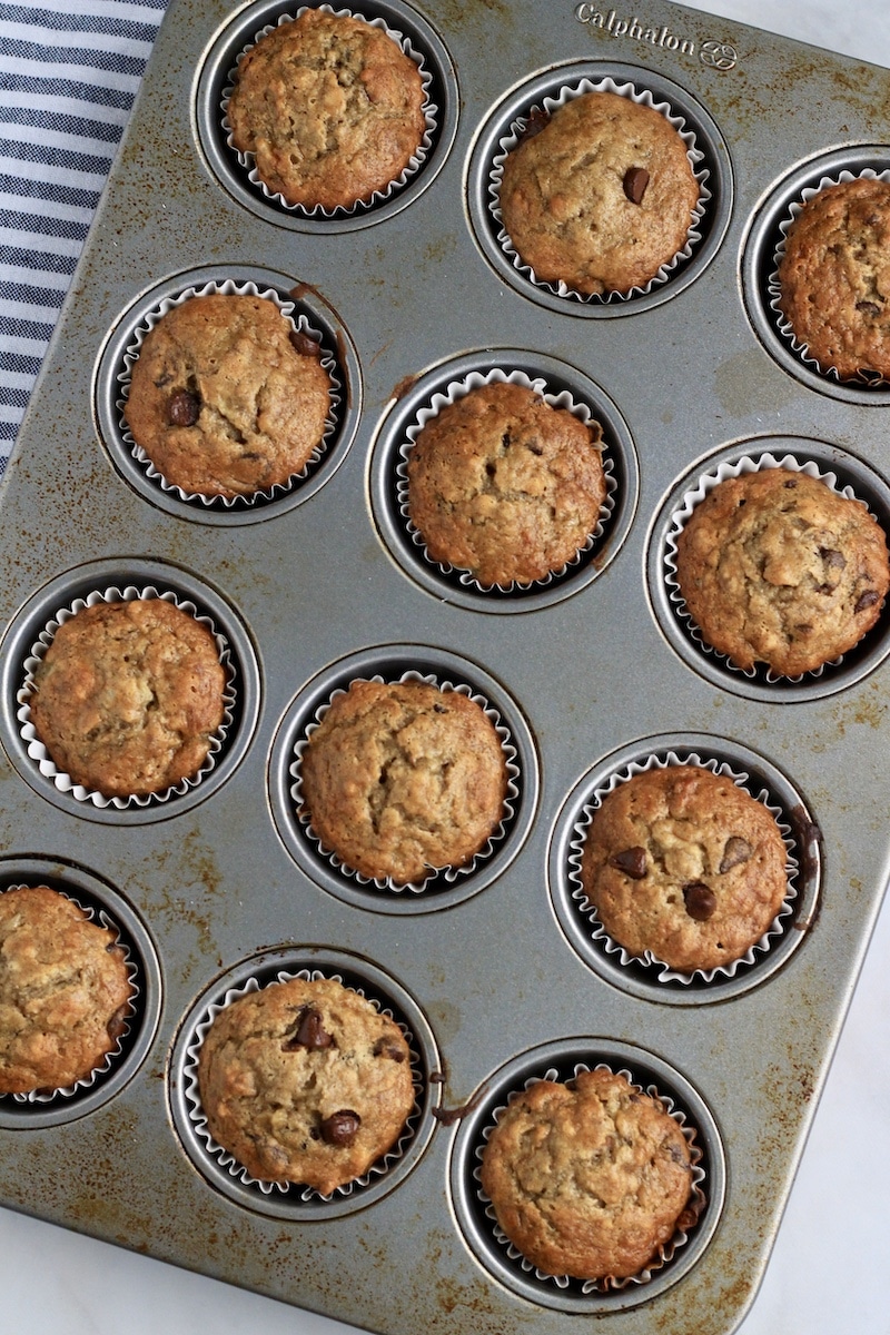 A standard muffin tin with chunky monkey muffins after baking.