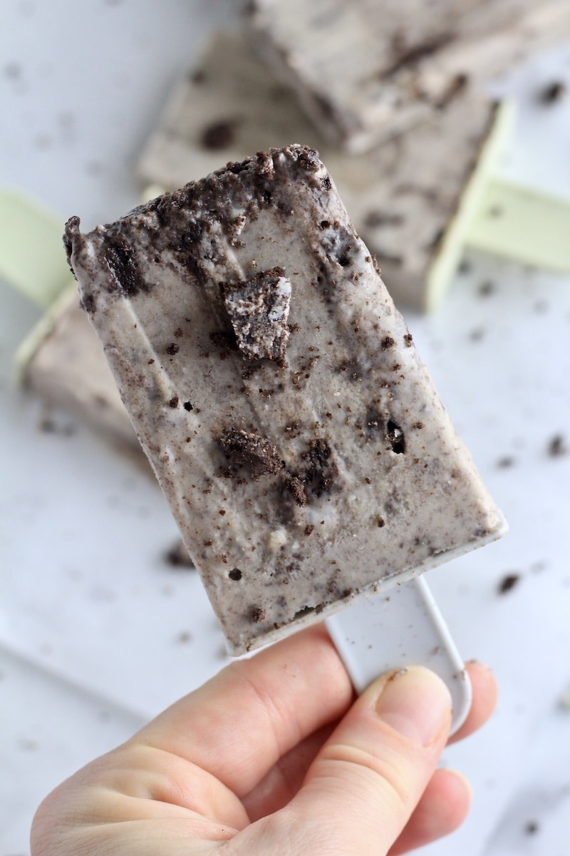A hand holding a cookies and cream popsicle with extra cookie crumbs.