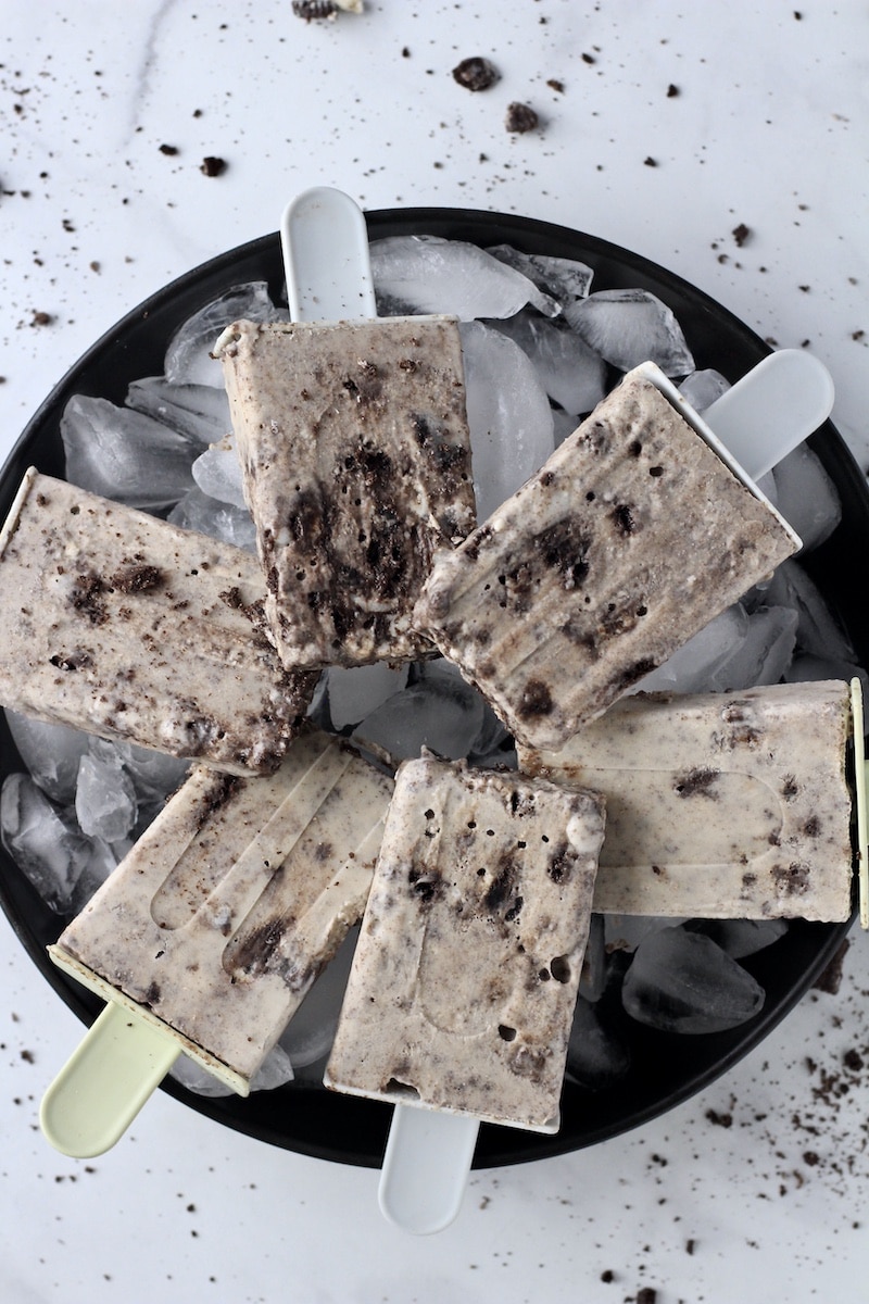 A black plate with ice cubes and cookies and cream popsicles.