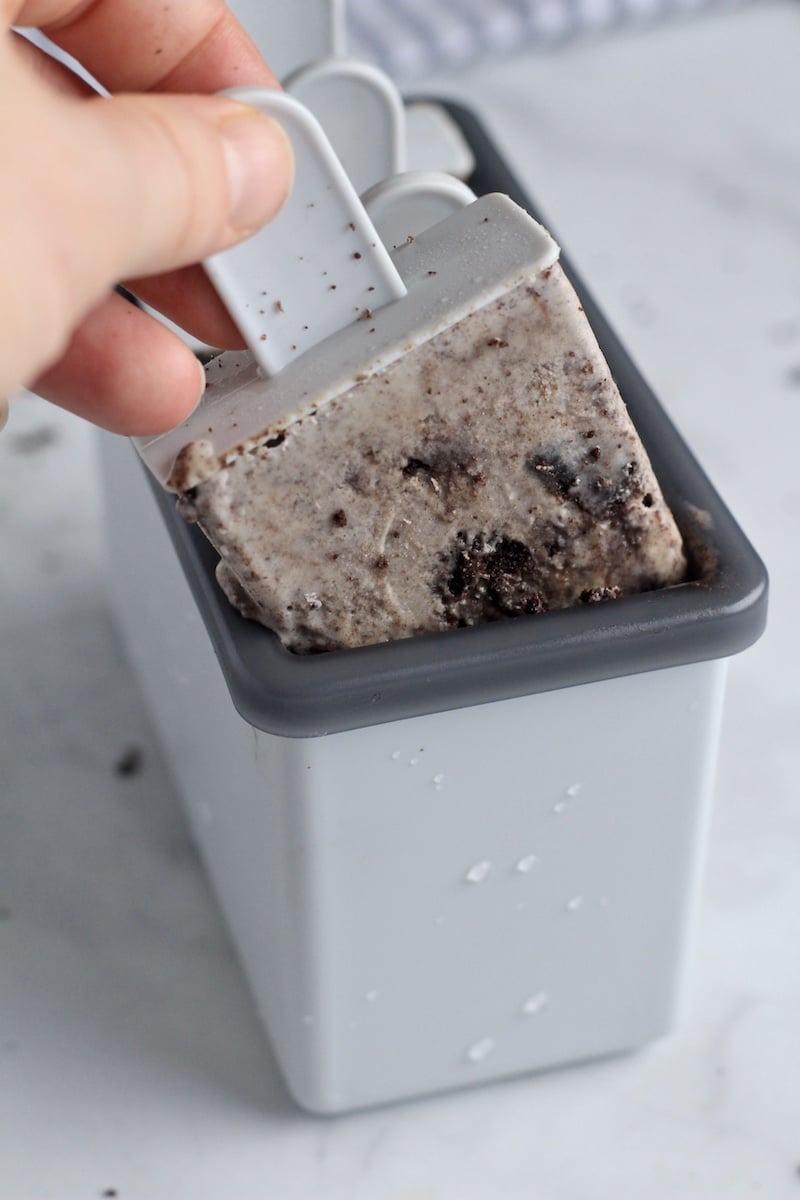 A hand pulling a cookies and cream popsicle out of the popsicle mold.