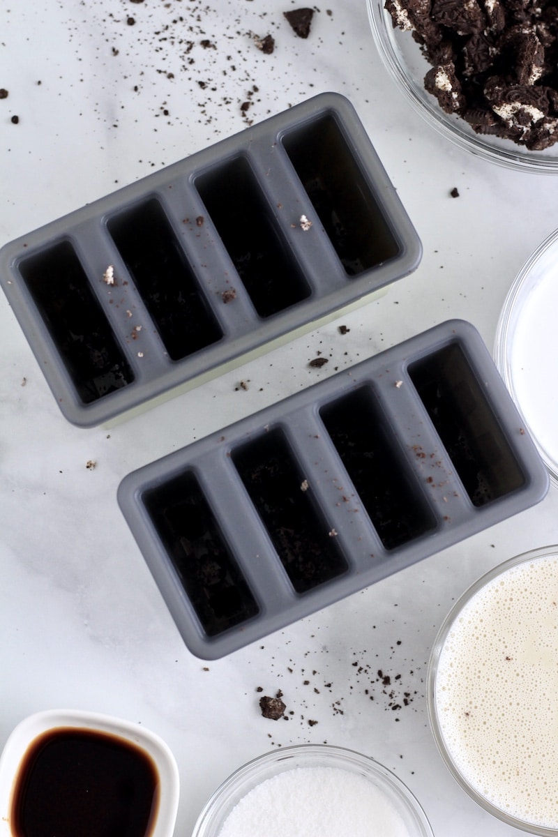 Popsicle molds with Oreo cookie crumbs sprinkled in and the other ingredients around the molds.