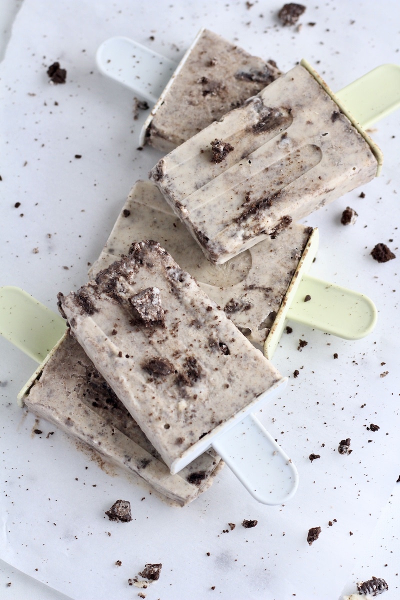 A stack of 5 cookies and cream popsicles on parchment paper with cookie crumbs around.