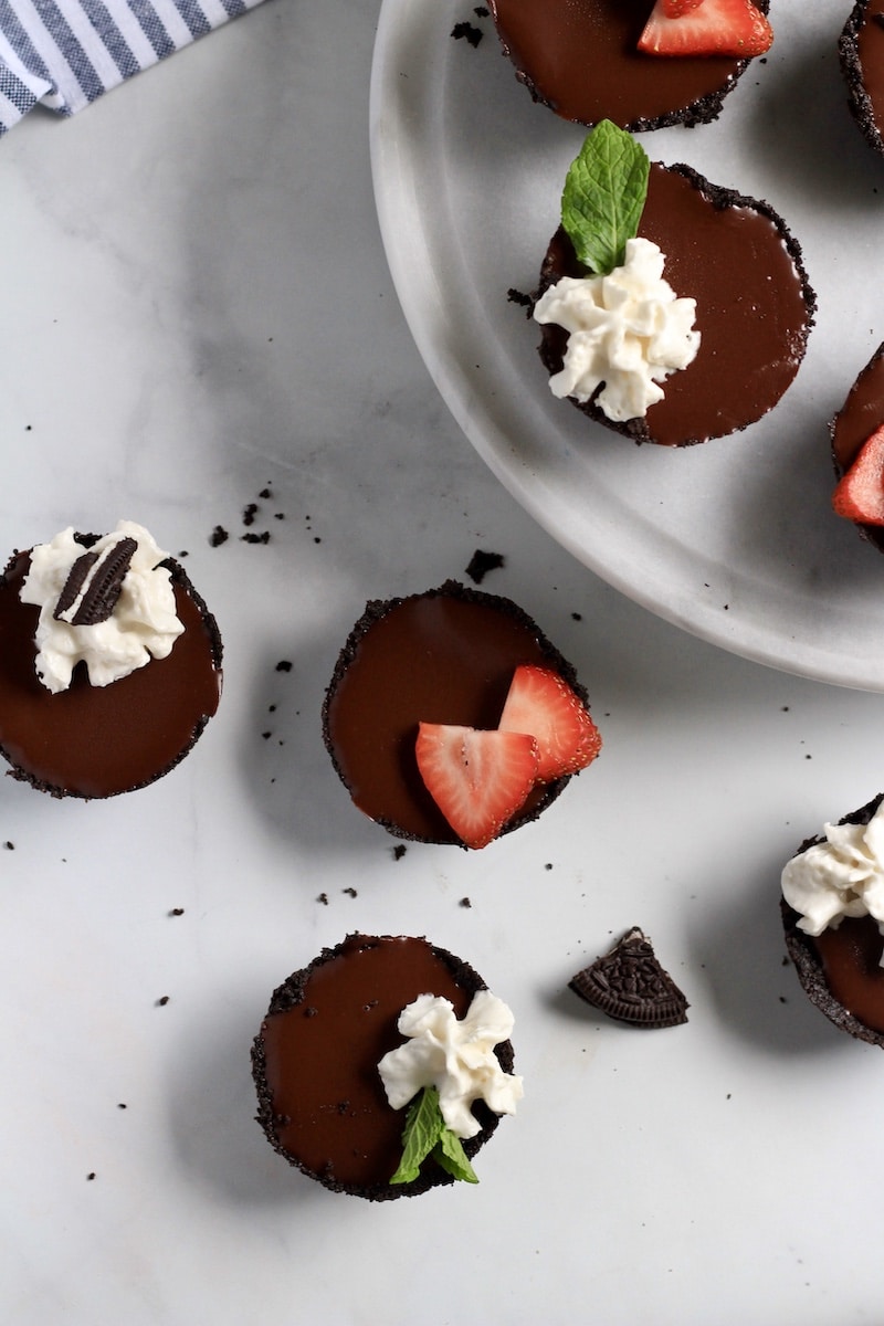 Top down photo of no-bake chocolate tarts with whipped cream and strawberries.