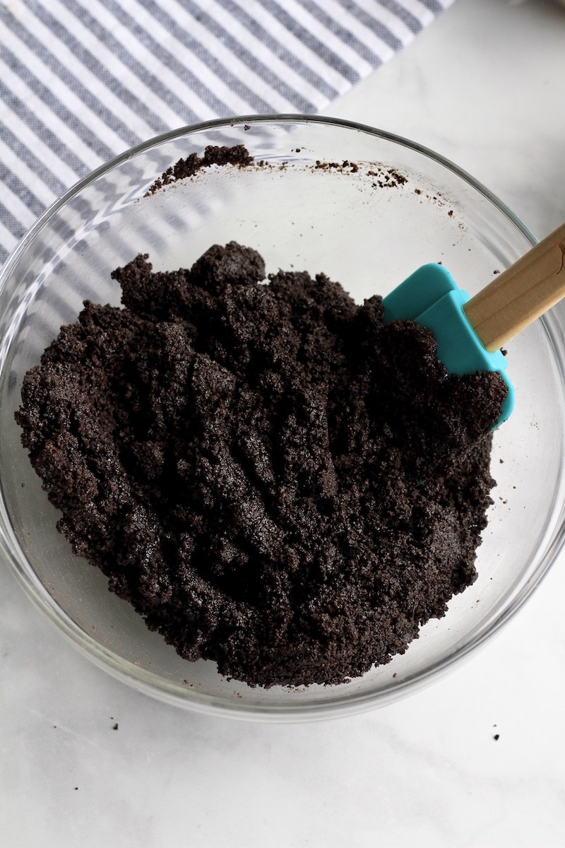A glass bowl with a rubber spatula after mixing the Oreo cookie crumbs with melted butter.