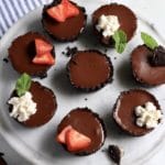 A marble plate with mini chocolate tarts topped with whipped topping and fruit.