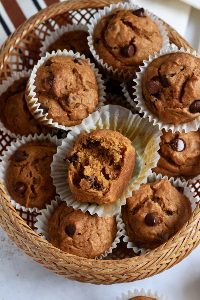 A brown basket filled with pumpkin muffins and the top muffin is peeled with a bite taken out.